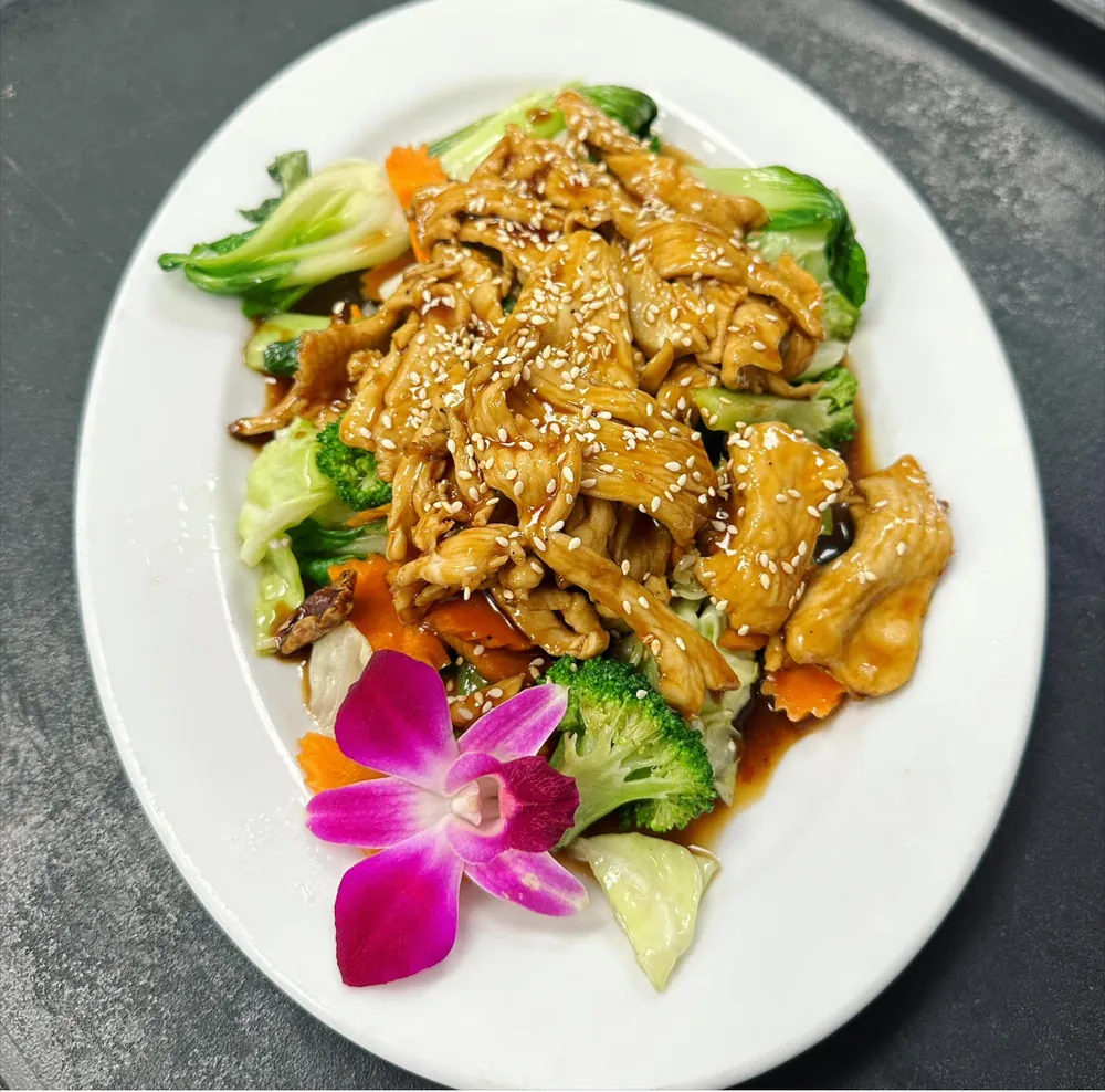 Sesame chicken over broccoli and carrots, garnished with an orchid